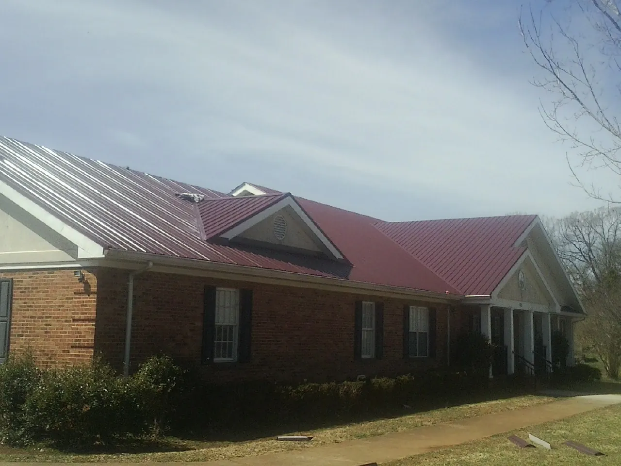 Red metal roof with gabled entries on a long brick building, from a Hail Damage Roof Repair job in Millerstown