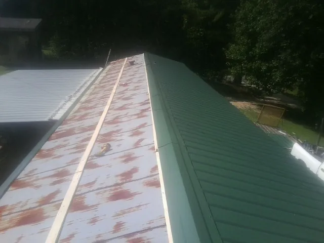 Old rusted panels beside newly installed green metal roofing in Millerstown