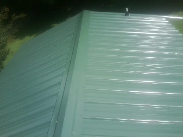 New green metal panels meeting at the ridge of a roof — Flat Roof Repair work by our crew in Millerstown