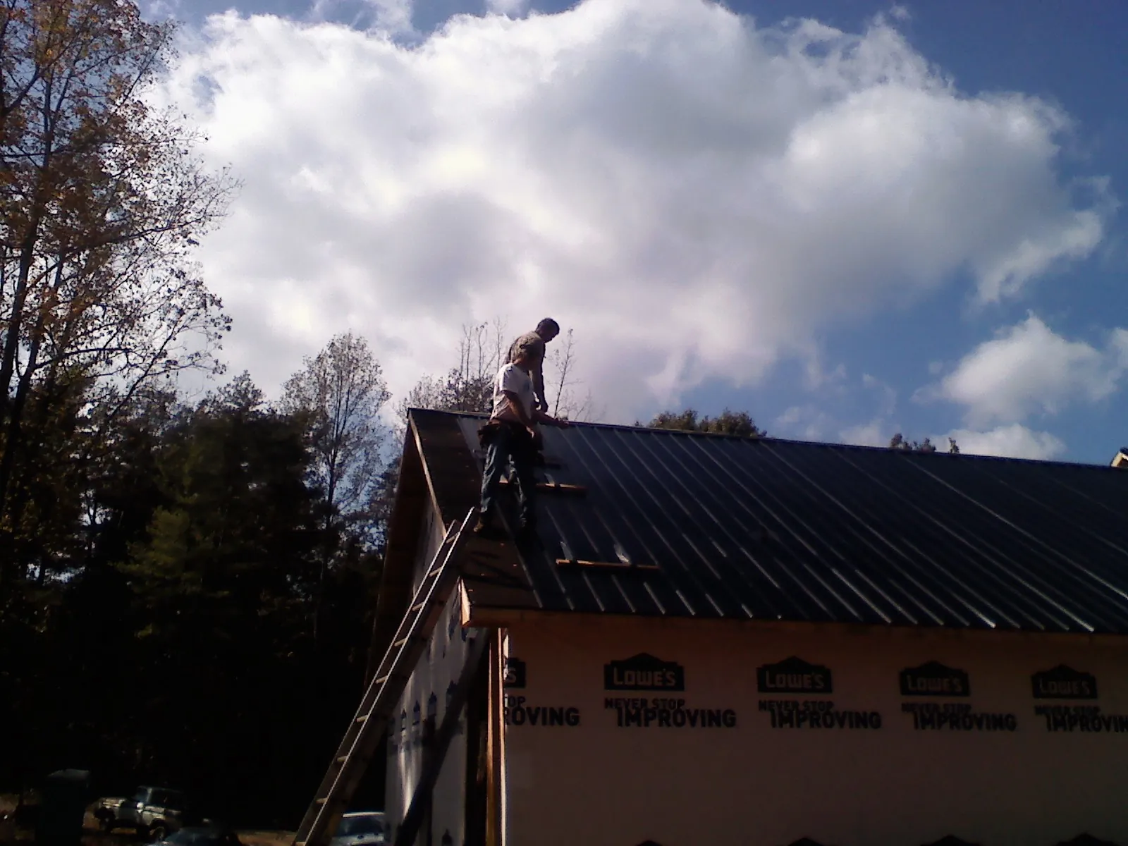 Roofer fastening dark metal panels high against a cloudy sky, from a Roof Inspection job in Millerstown