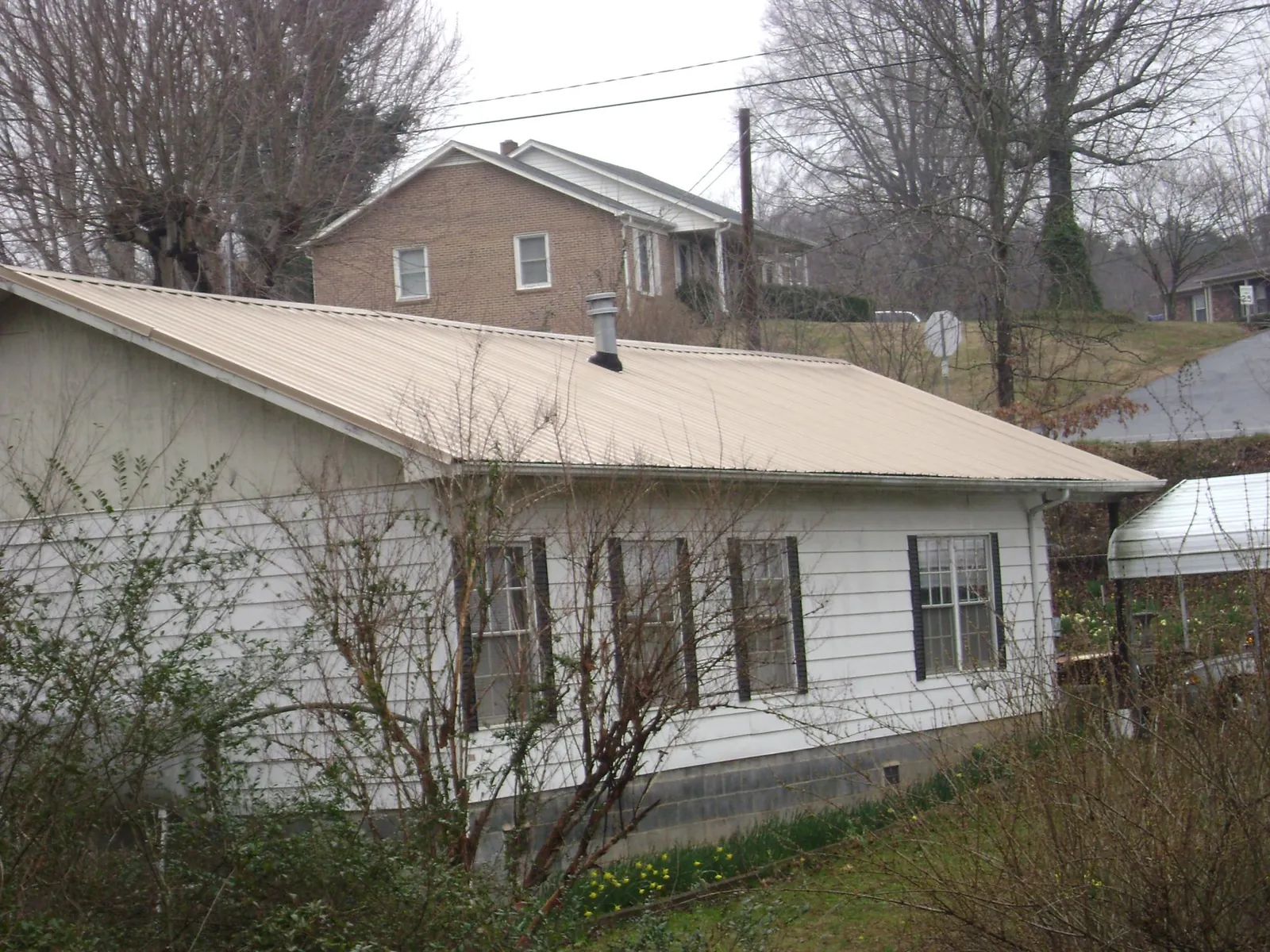 Tan metal roof on a white sided house set into a hillside — Commercial Roofing by Roofing Brothers in Millerstown